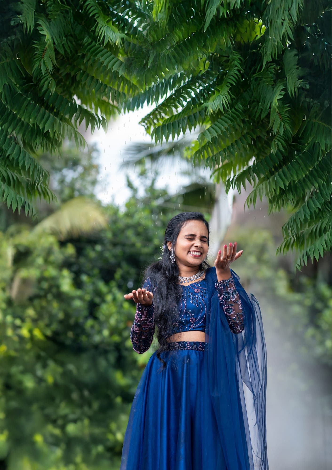 Woman in a beaded blue outfit catching rain, laughing joyfully