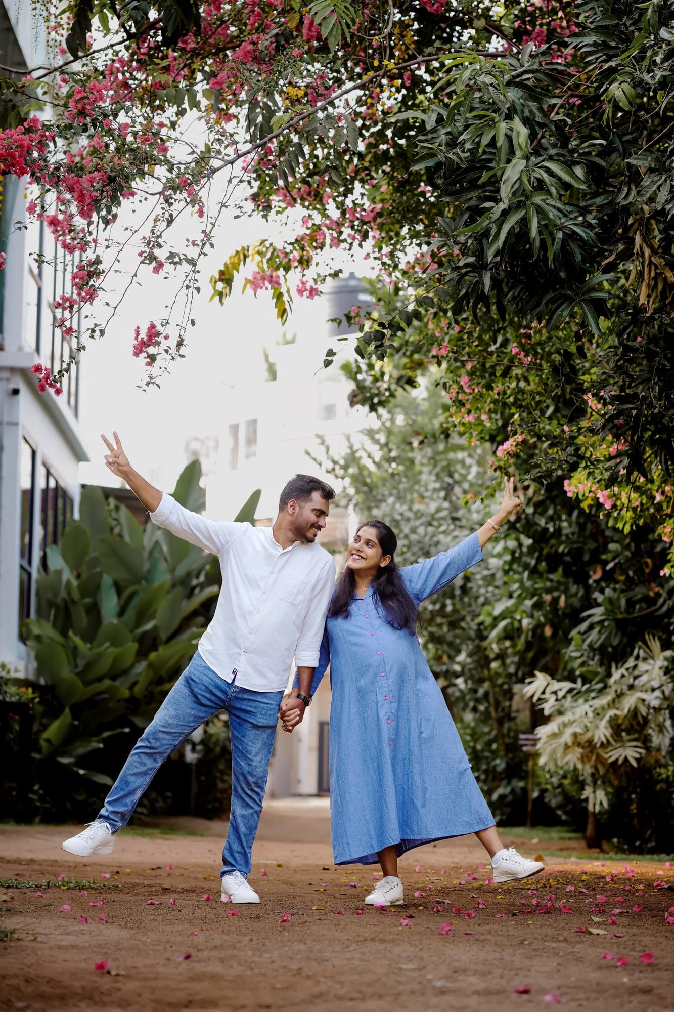 Expecting couple joyfully posing under blossoming trees