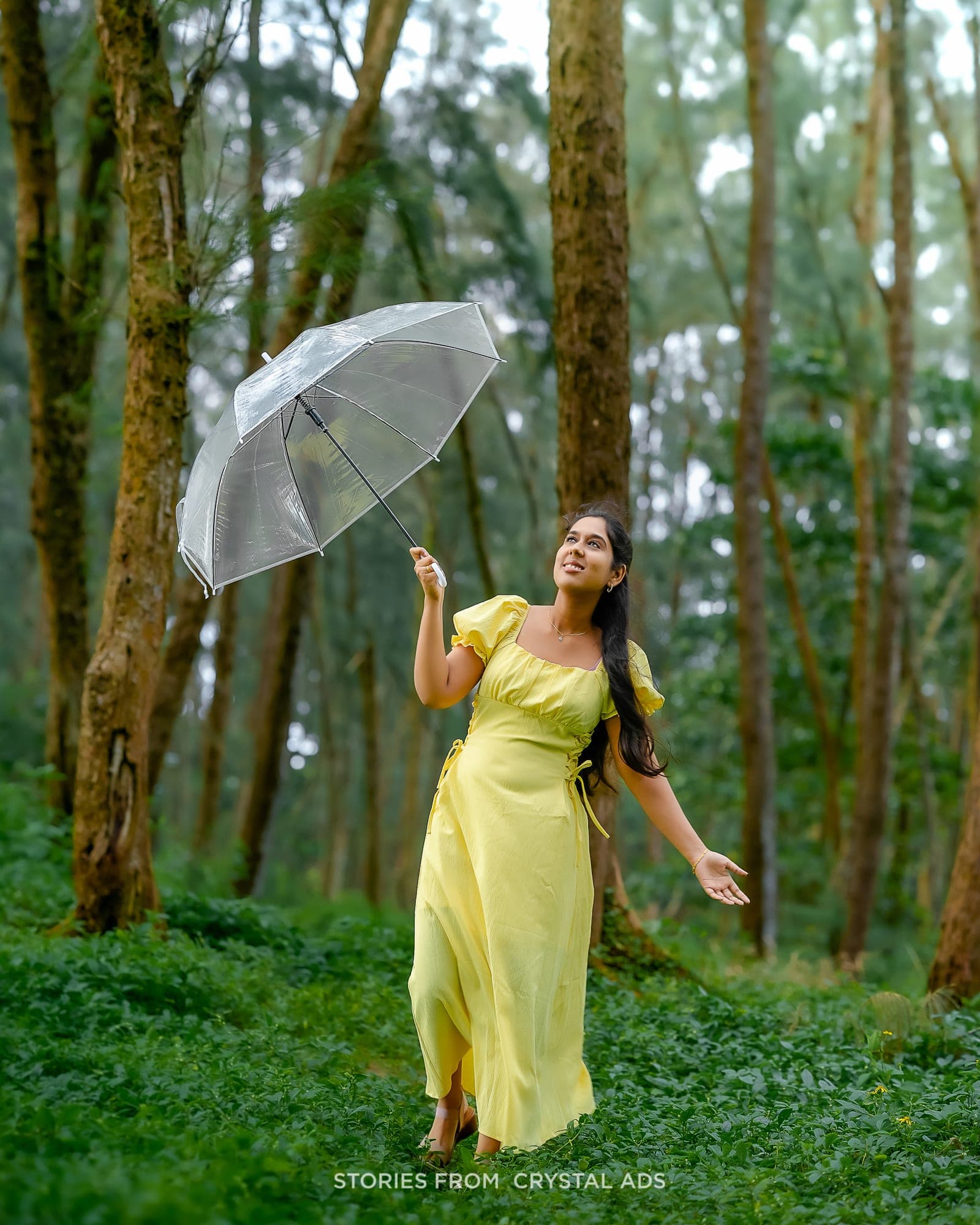 Woman in a yellow dress holding a clear umbrella in a forest