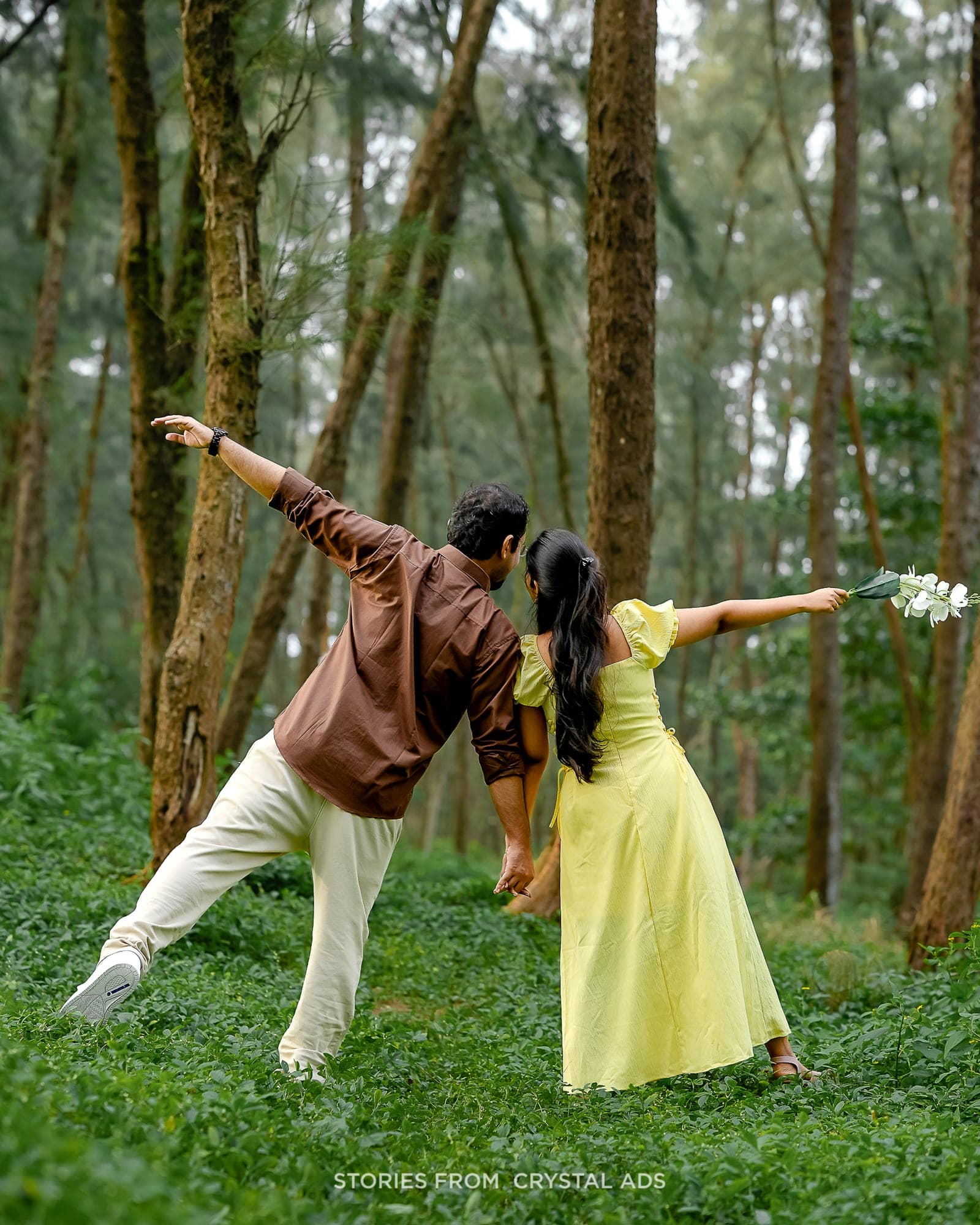 Couple playfully posing together in a forest, seen from behind