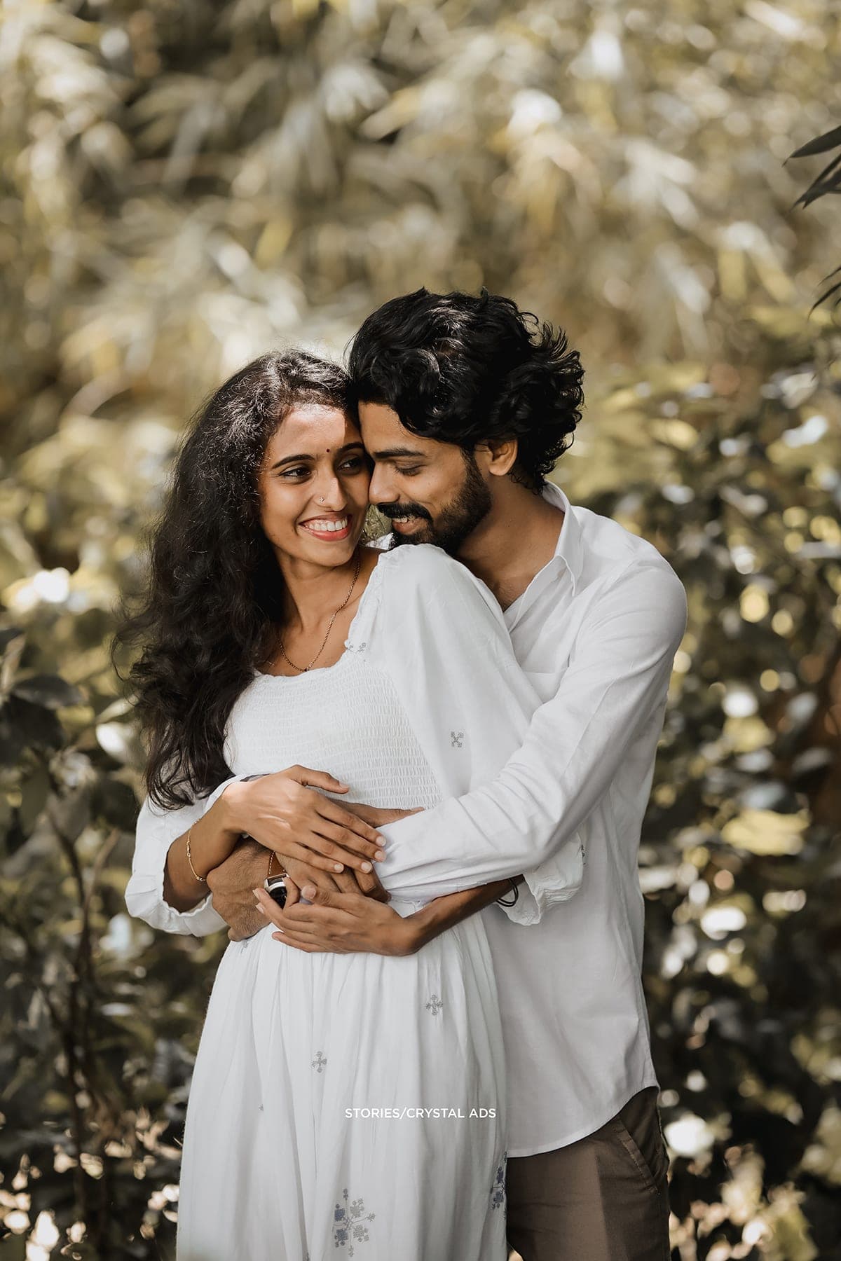 He embraces her from behind among sunlit leaves