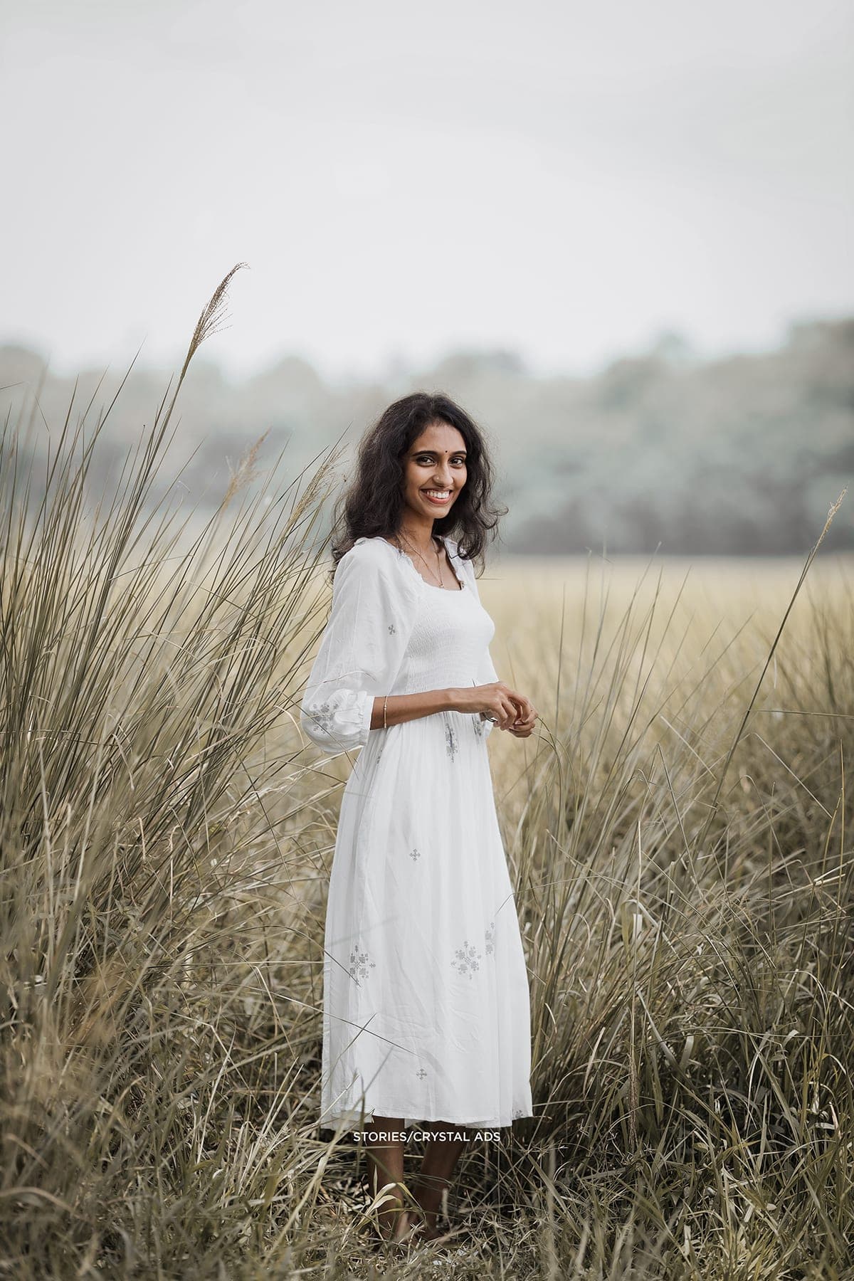 She stands alone in tall grass in a white dress