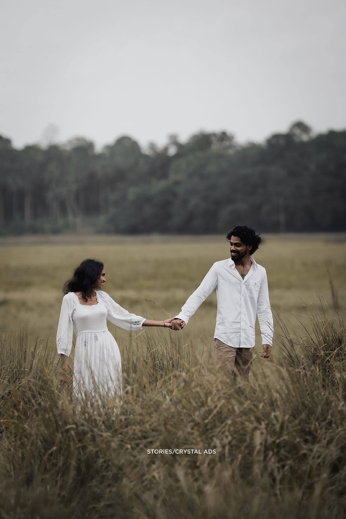Couple hand in hand in a field with trees behind
