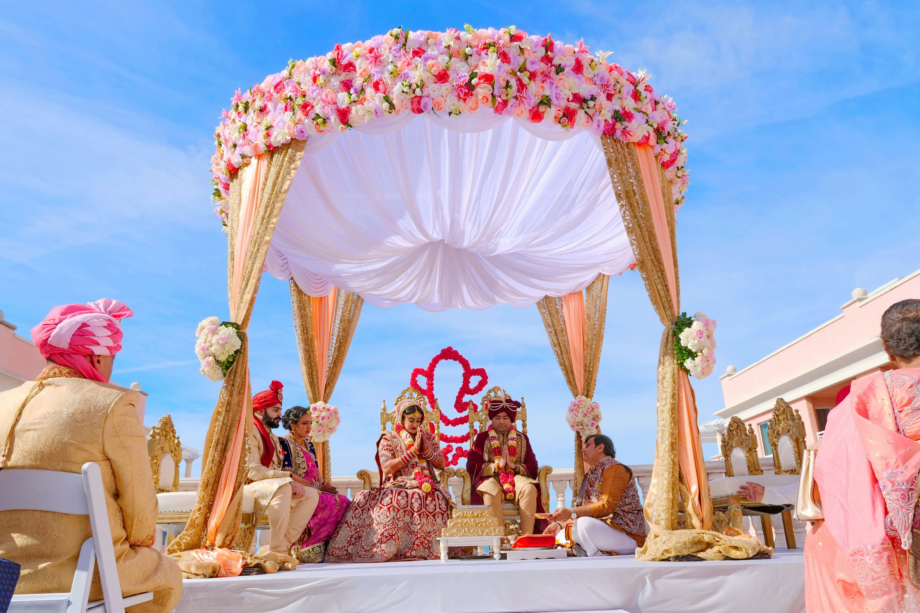 A couple seated together during a traditional wedding ceremony under a floral canopy