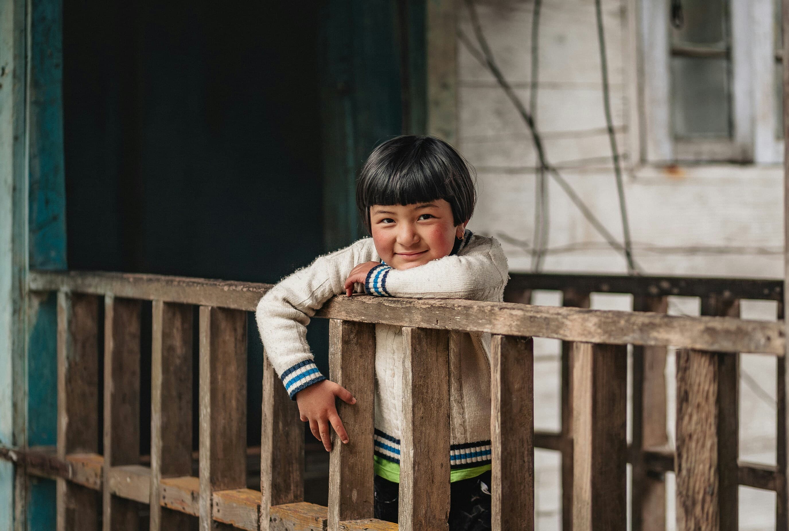 Young child smiling from behind a wooden railing